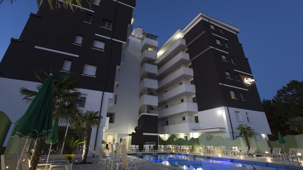 Ein mehrstöckiges Hotel mit Schwimmbad, Außenbereich und Palmen.