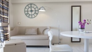 Ein modernes Wohnzimmer mit einer Couch, einem weißen Sessel, einem runden Tisch, einer Stehlampe, einer Uhr und einer Vase mit Blumen.