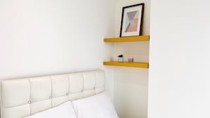 Een bed met een gestoffeerd hoofdbord, wit beddengoed en een klein, ingelijst fotootje op een plank erboven.
