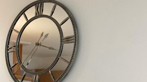 Een ronde wandklok met Romeinse cijfers en een spiegelende oppervlakte.