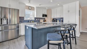 A modern kitchen with white cabinets, stainless steel appliances, a blue island, and black bar stools.