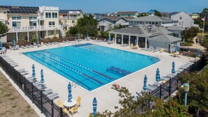 A large rectangular swimming pool surrounded by lounge chairs and umbrellas, with a view of residential buildings in the background.