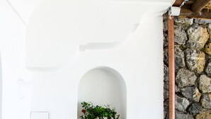 Pared blanca con un arco de piedra, un lavabo de piedra, una botella verde y una planta en maceta.