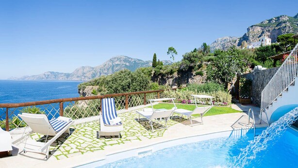 Zona de piscina con sillones de descanso y vistas al mar.