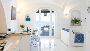 Un salón luminoso y espacioso con vistas al mar, un comedor con mesa para dos, y una zona de estar acogedora con un plaid estampado.