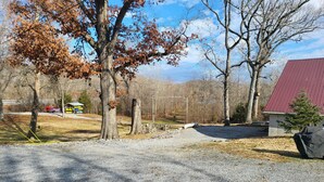 A gravel driveway leading to a building with a red roof, surrounded by trees and a clear sky. - Clean, full kitchen, stand alone cabin adjoining Lake Barkley State Park (Cadiz)