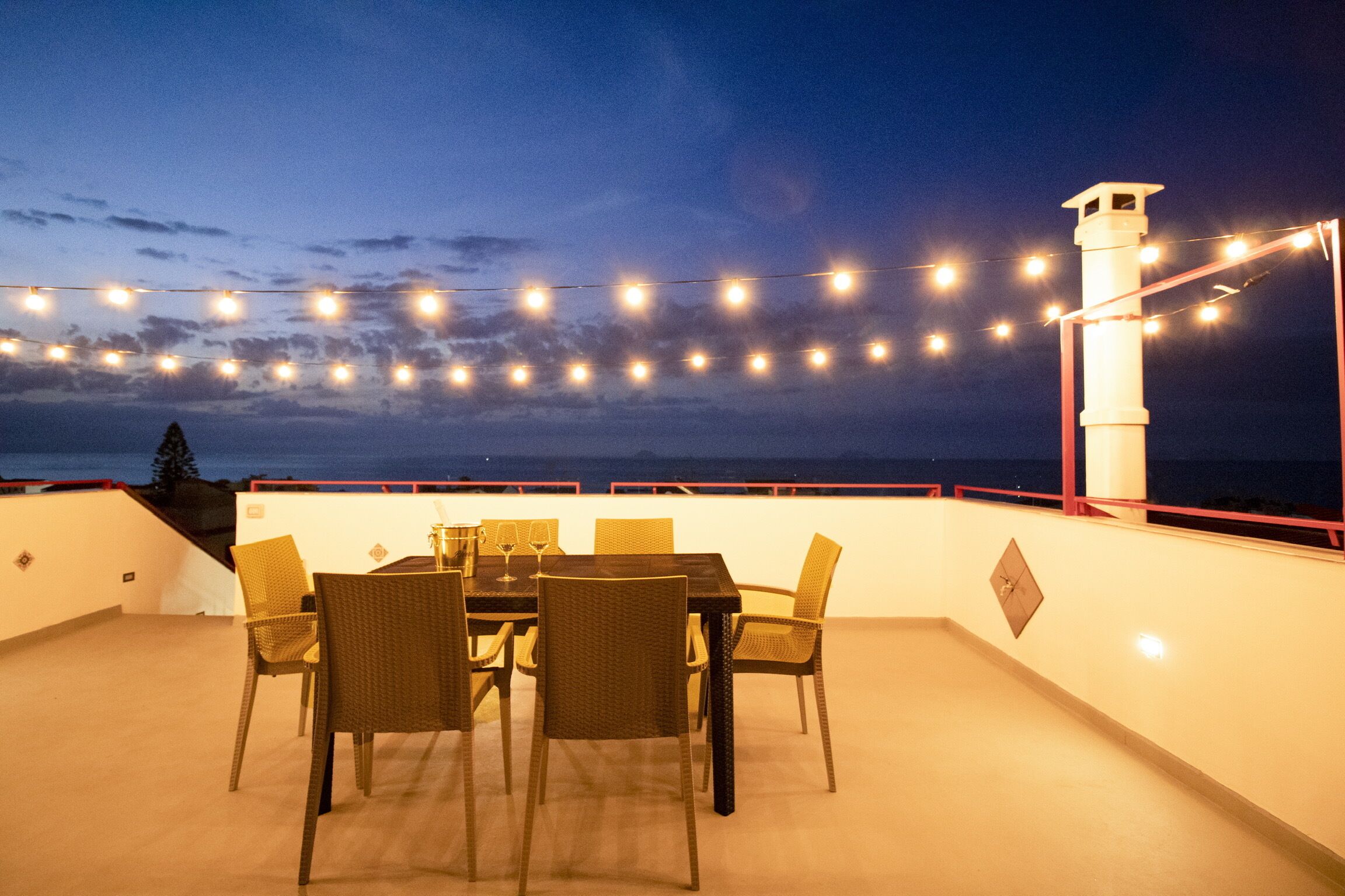 Une terrasse sur le toit, avec une table et des chaises, des guirlandes lumineuses et un phare en arrière-plan.
