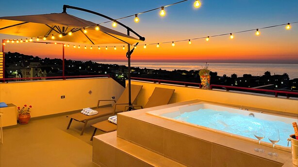 A rooftop terrace with a hot tub, lounge chairs, and string lights against a sunset view. - Duke of Aosta Terrace with private mini-pool (Acquedolci)