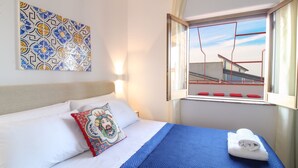 A hotel room with a bed, a decorative wall piece, a window with a view of a building, and a towel on the bed. - Duke of Aosta Terrace with private mini-pool (Acquedolci)