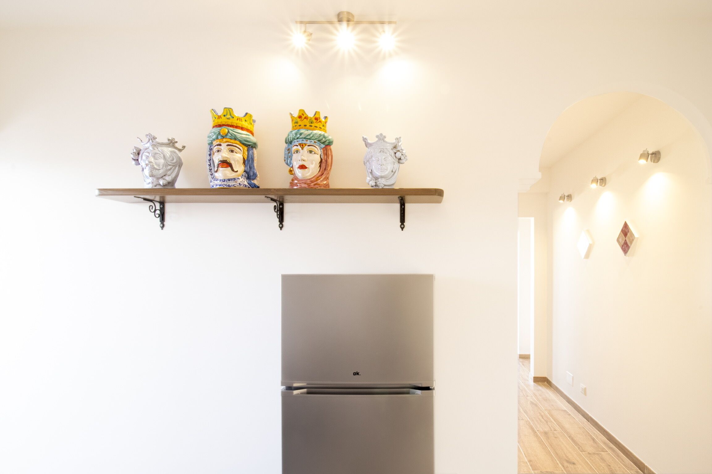 Eine Küche mit einem modernen Kühlschrank, einem Regal mit Dekoration und einem Flur mit Beleuchtung.