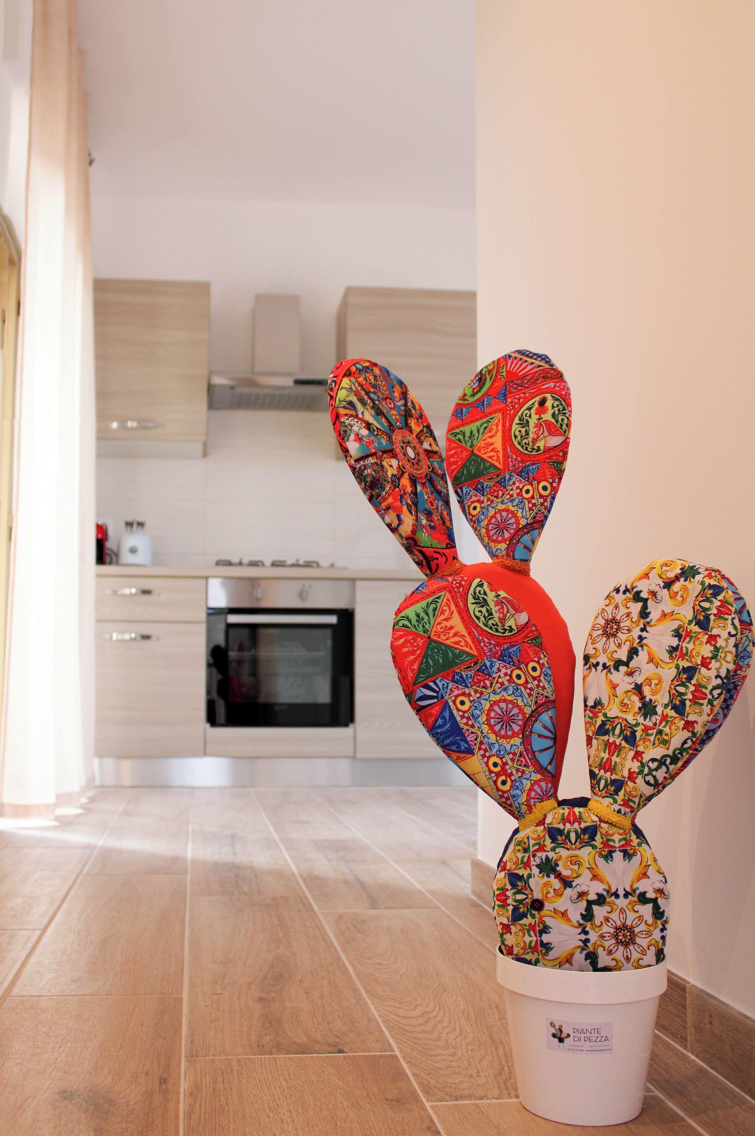A cactus plant in a white pot with a colorful design, placed in a kitchen with light wooden cabinets and a stainless steel oven.
