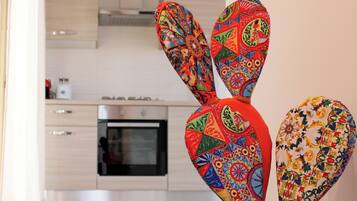 A cactus plant in a white pot with a colorful design, placed in a kitchen with light wooden cabinets and a stainless steel oven.