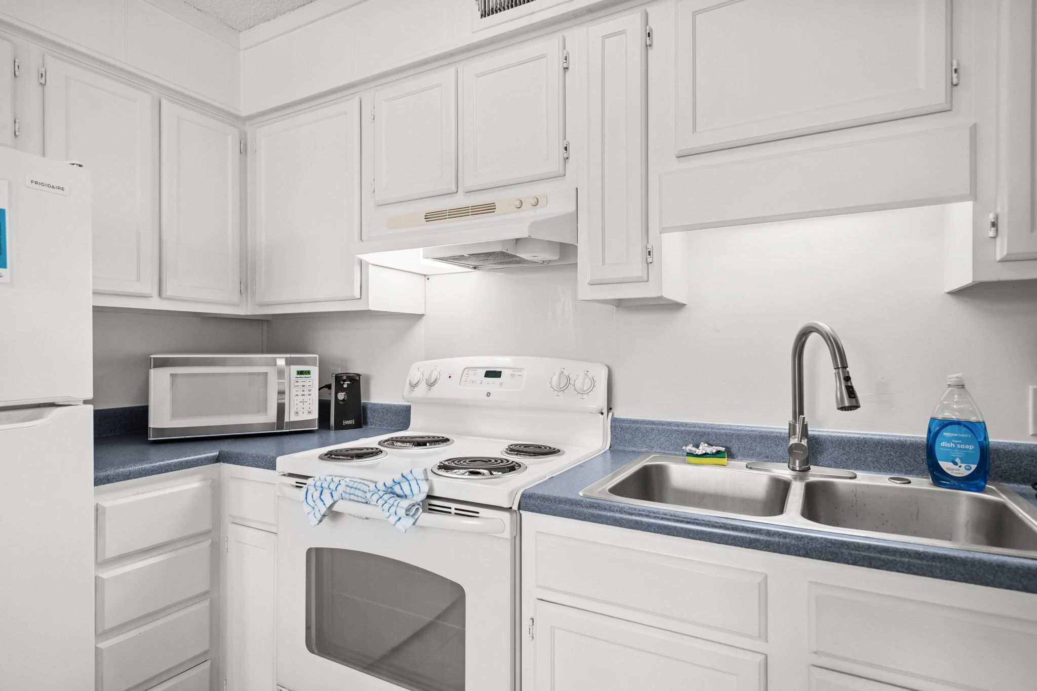 A kitchen with white cabinets, a microwave, a stove, and a sink.