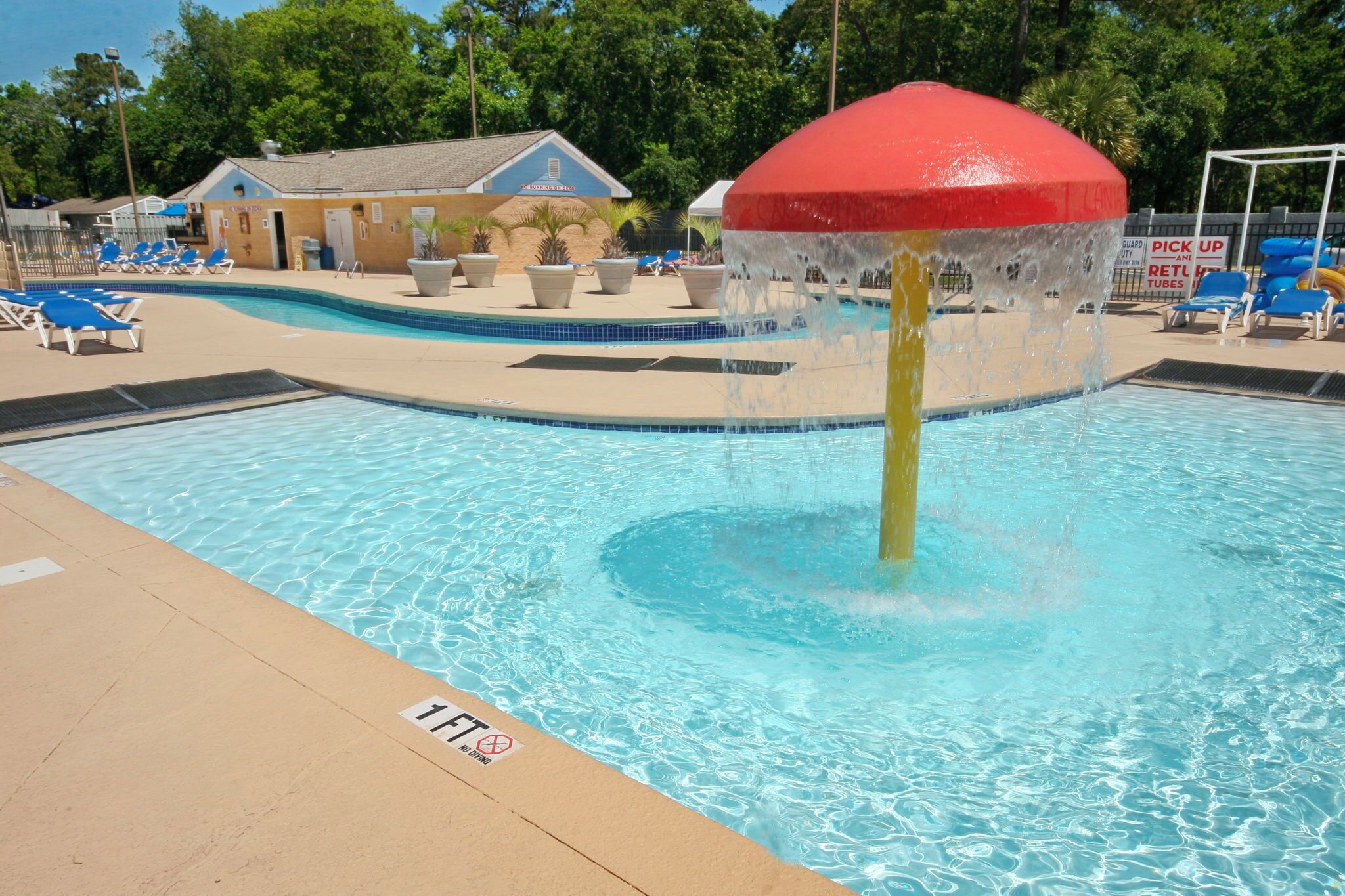Una piscina con fuente, sillones de descanso y un edificio al fondo.