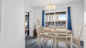 Un comedor con una mesa y sillas de madera, una araña y vistas a un edificio a través de una ventana con cortinas azules.