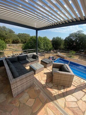 Une terrasse extérieure avec des meubles en osier, un sol en pierre et une piscine.