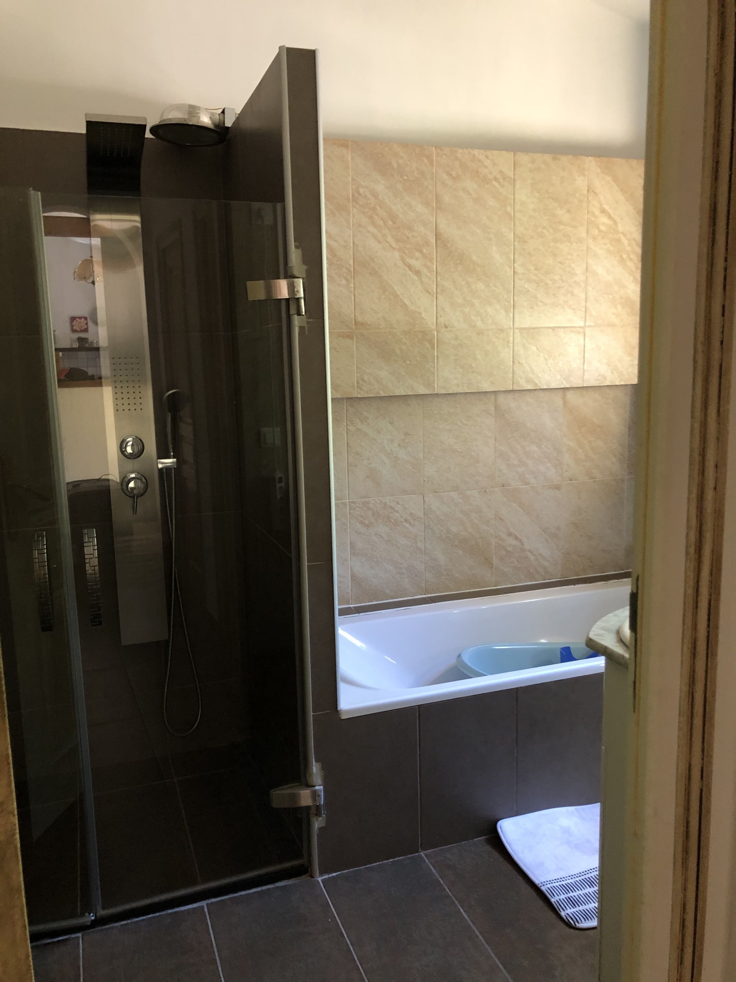 A modern bathroom with a glass-enclosed shower, a bathtub, and beige tiled walls.