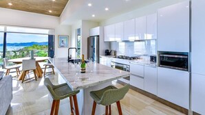 A modern kitchen with white cabinets, a marble island, and a view of the sea.