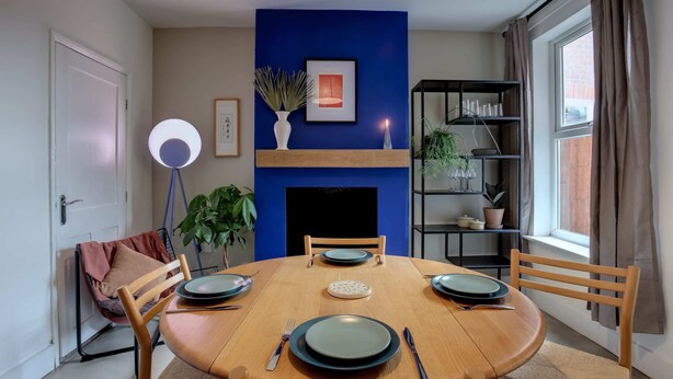 Zona pranzo con tavolo rotondo in legno, quattro sedie e una parete decorata in blu.