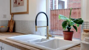 Una cucina con un lavello bianco, un rubinetto nero, una pianta in vaso e un quadro appeso al muro.