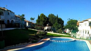 Une piscine dotée d’une terrasse carrelée, entourée de verdure et de bâtiments.