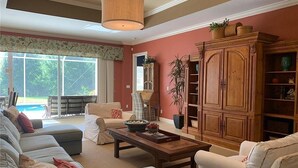 A spacious living room with a large sectional sofa, a wooden cabinet, and a dining table.