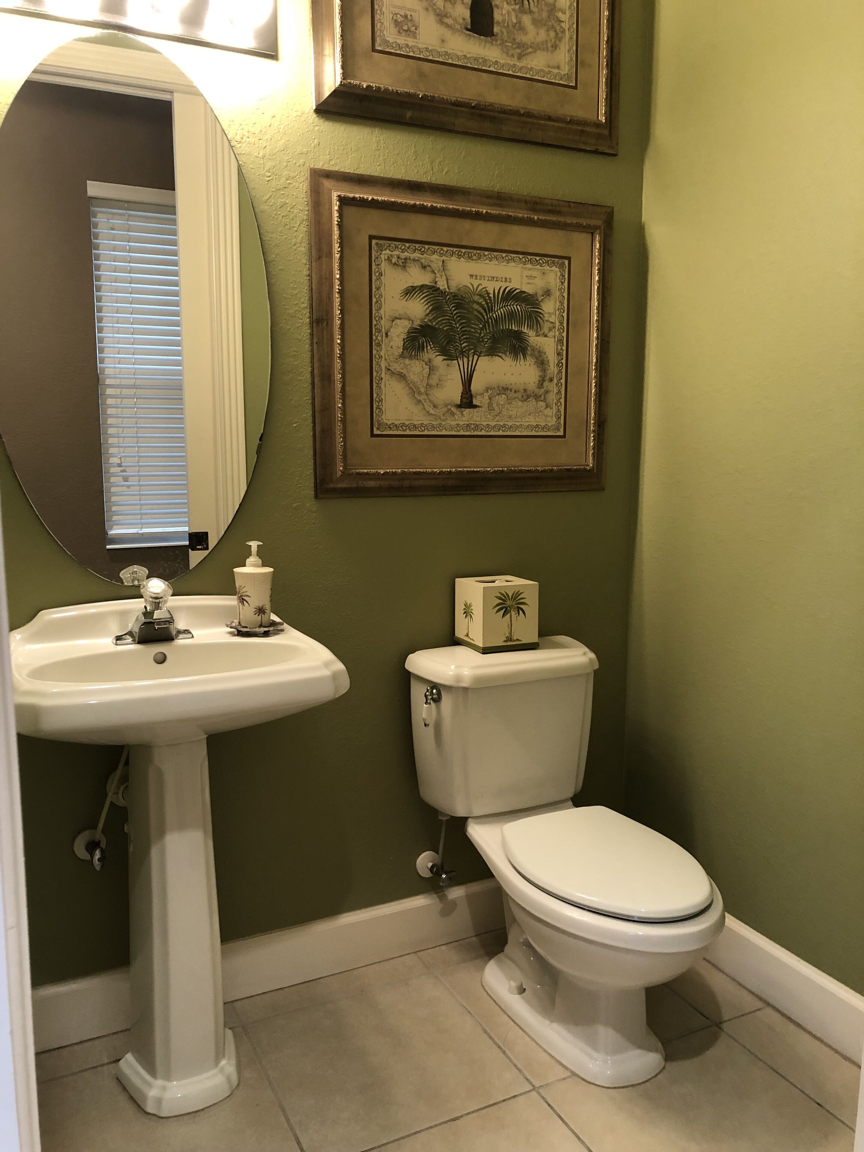 A bathroom with a pedestal sink, toilet, and framed artwork on the wall.