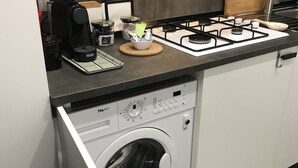 A compact kitchen with a built-in washer and dryer, a coffee maker, and a gas stove. - Ade Home (Catania)