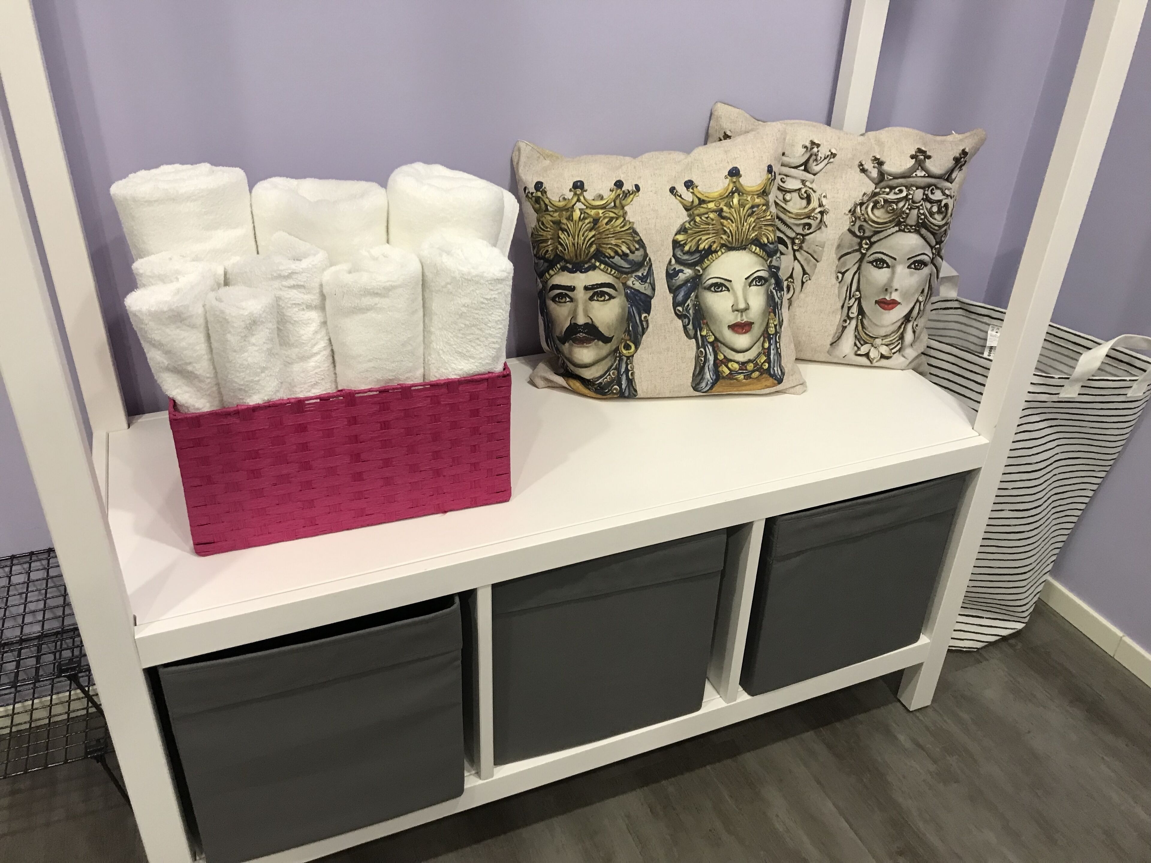 A storage unit with a pink basket and decorative pillows.