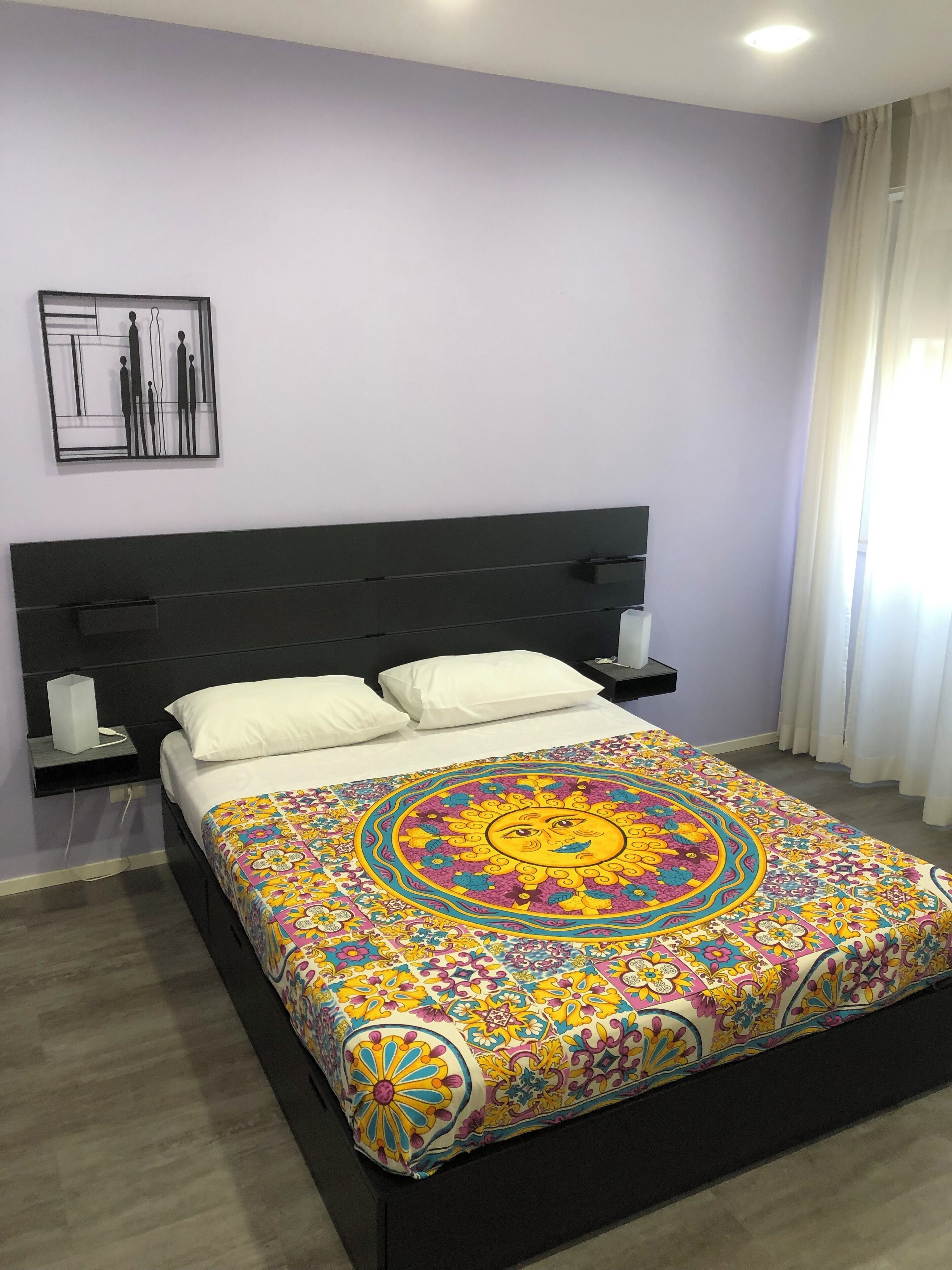 Quarto com cama, duas mesas de cabeceira, um criado-mudo, uma obra de arte na parede e janela com cortinas.
