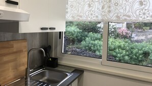 A modern kitchen with white cabinets, a stainless steel sink, and a window overlooking a garden with various plants and flowers. - Ade Home (Catania)