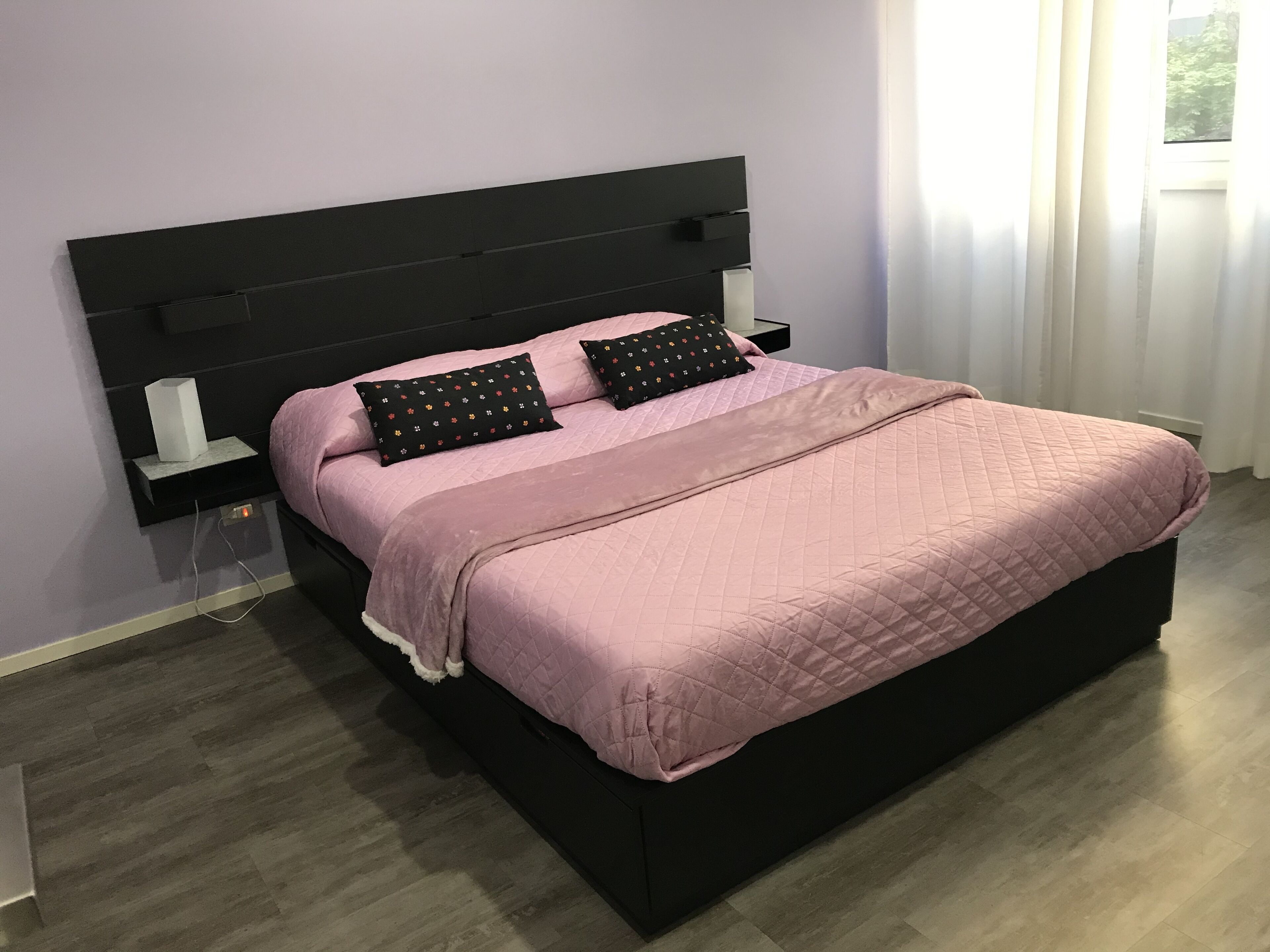 A modern bedroom with a black headboard, a pink quilted bedspread, and two decorative pillows.