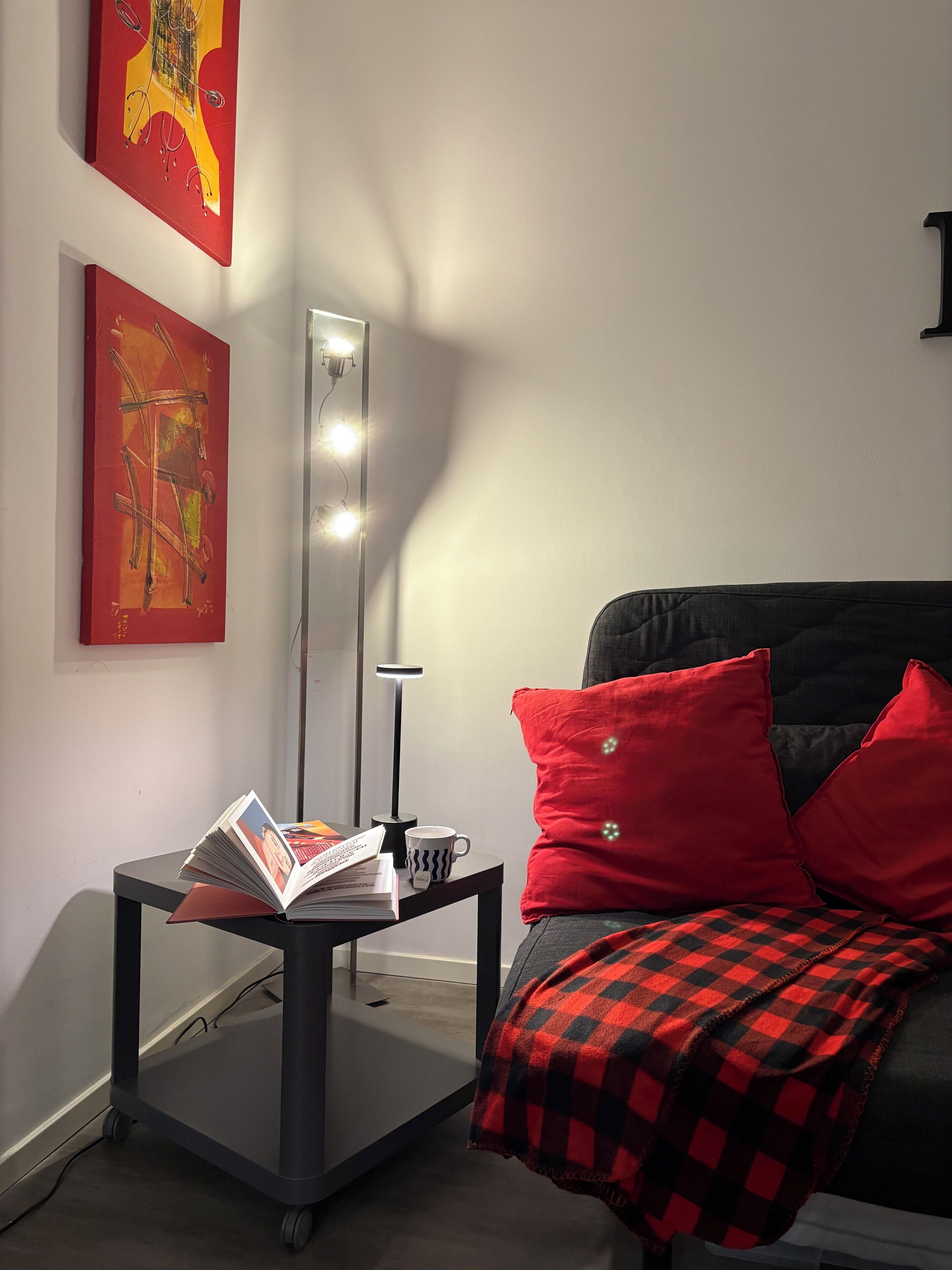 Une chambre à coucher moderne avec un lit, une table de chevet sur laquelle se trouvent un livre et une tasse, une lampe sur pied et deux tableaux abstraits accrochés au mur.