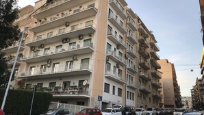A multi-story residential building with balconies, air conditioning units, and a street view with parked cars. - Ade Home (Catania)