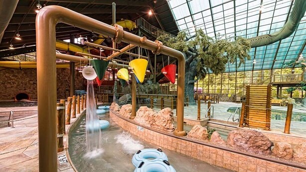 An indoor water play area with multiple slides and water features, surrounded by stone walls and a glass ceiling. - Celebrate July 4th in the beautiful Smoky mountains!! (Gatlinburg)
