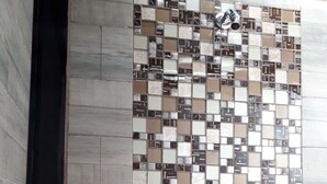 A bathroom with a tiled wall featuring a variety of square tiles in different shades of brown and beige. There are two metallic towel racks installed on the wall. - CIUDAD DE MEXICO UNAM GUEST HOUSE (Ciudad de México)