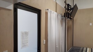 A room with a closed door, a white curtain, a bed with striped bedding, and a mounted television. - CIUDAD DE MEXICO UNAM GUEST HOUSE (Ciudad de México)