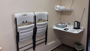 A small bathroom with two white chairs, a towel rack, a shelf with a kettle, a trash bin, and a small table with a bottle and a remote control. - CIUDAD DE MEXICO UNAM GUEST HOUSE (Ciudad de México)
