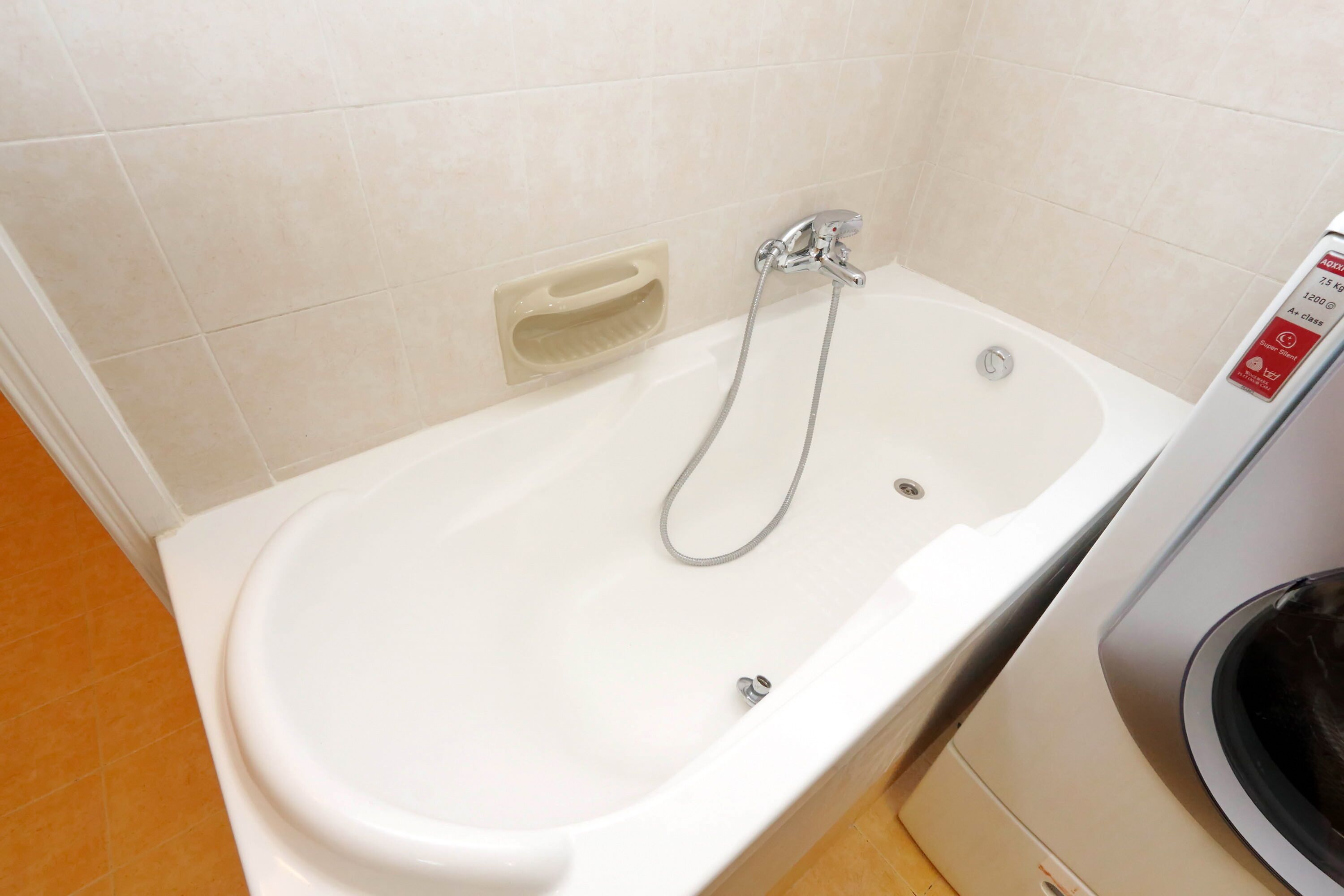 Un bagno con una vasca da bagno bianca, una doccetta e una lavatrice.