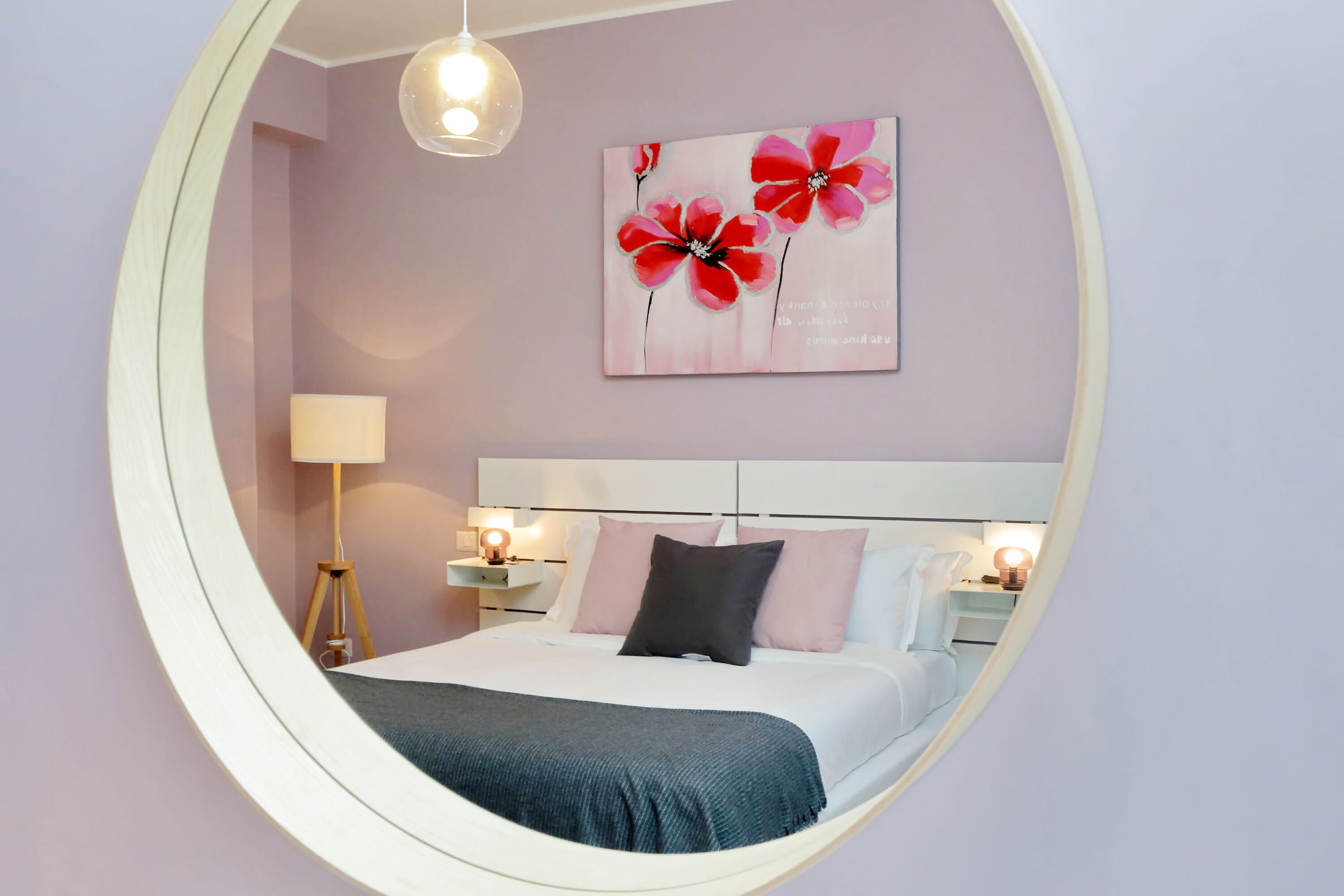 Un miroir rond reflète une chambre à coucher avec un lit, des lampes de chevet et un tableau accroché au mur.