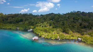 An aerial view of a tropical island with clear turquoise waters, lush greenery, and several small wooden structures connected by walkways.