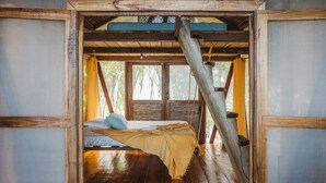 A rustic wooden room with a bed, a window, and a wooden ceiling structure.