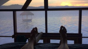 A person lying on a bed with a view of the sunset over water.