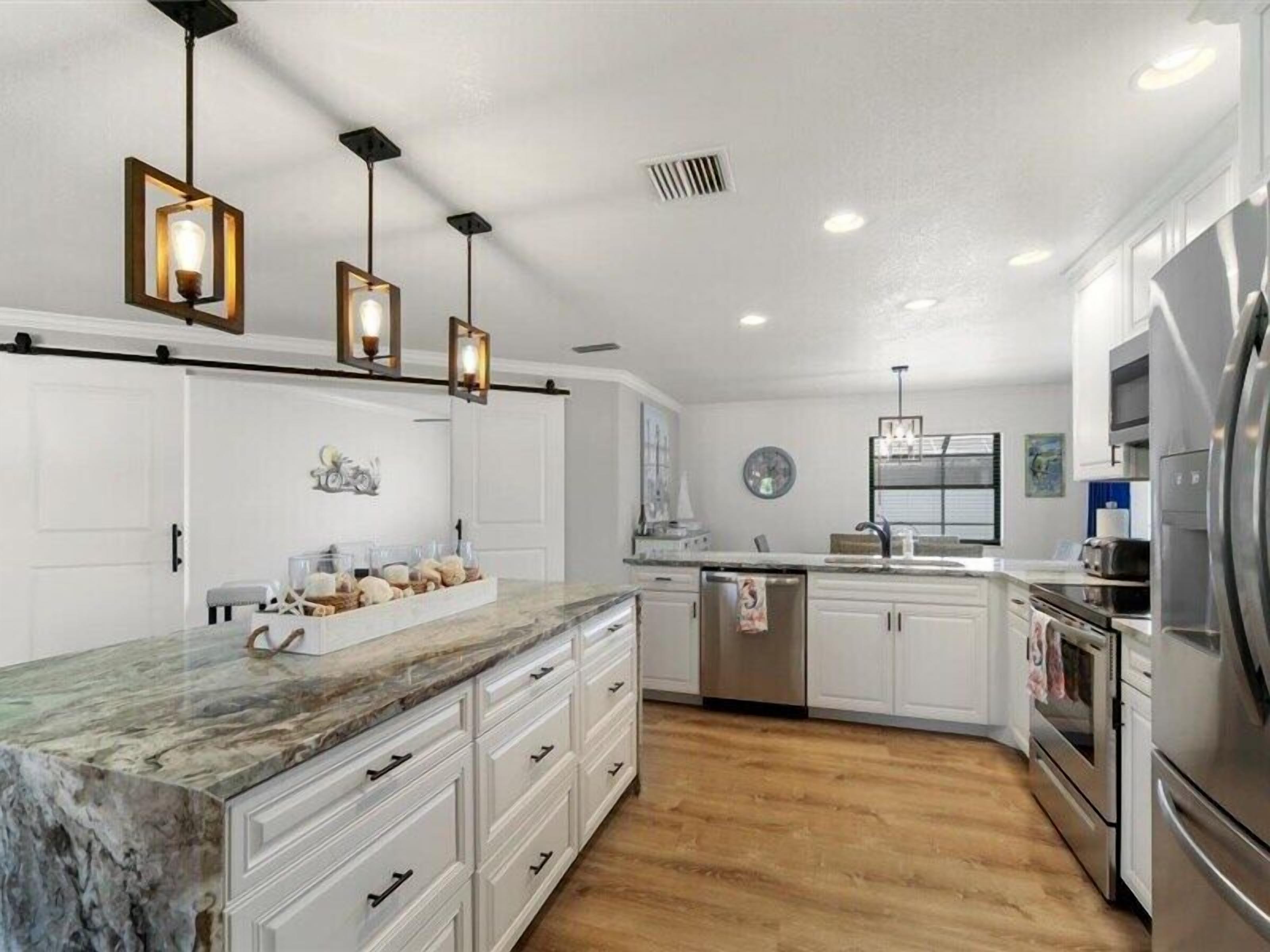 A modern kitchen with white cabinets, a marble countertop, stainless steel appliances, and pendant lighting.