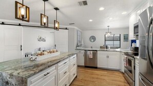 A modern kitchen with white cabinets, a marble countertop, stainless steel appliances, and pendant lighting. - Turquoise Turtle - pool and spa, beautifully furnished (Englewood)