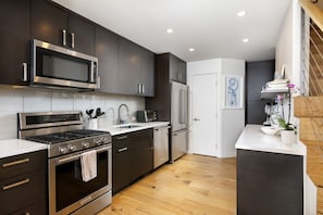 A modern kitchen with dark cabinetry, stainless steel appliances, and a wooden floor. - Downtown Aspen Townhome—Minutes to Gondola/Art Museum (Aspen)