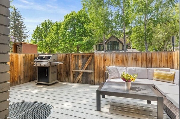 An outdoor deck with a barbecue grill, a wooden fence, and a sofa with cushions. - Downtown Aspen Townhome—Minutes to Gondola/Art Museum (Aspen)