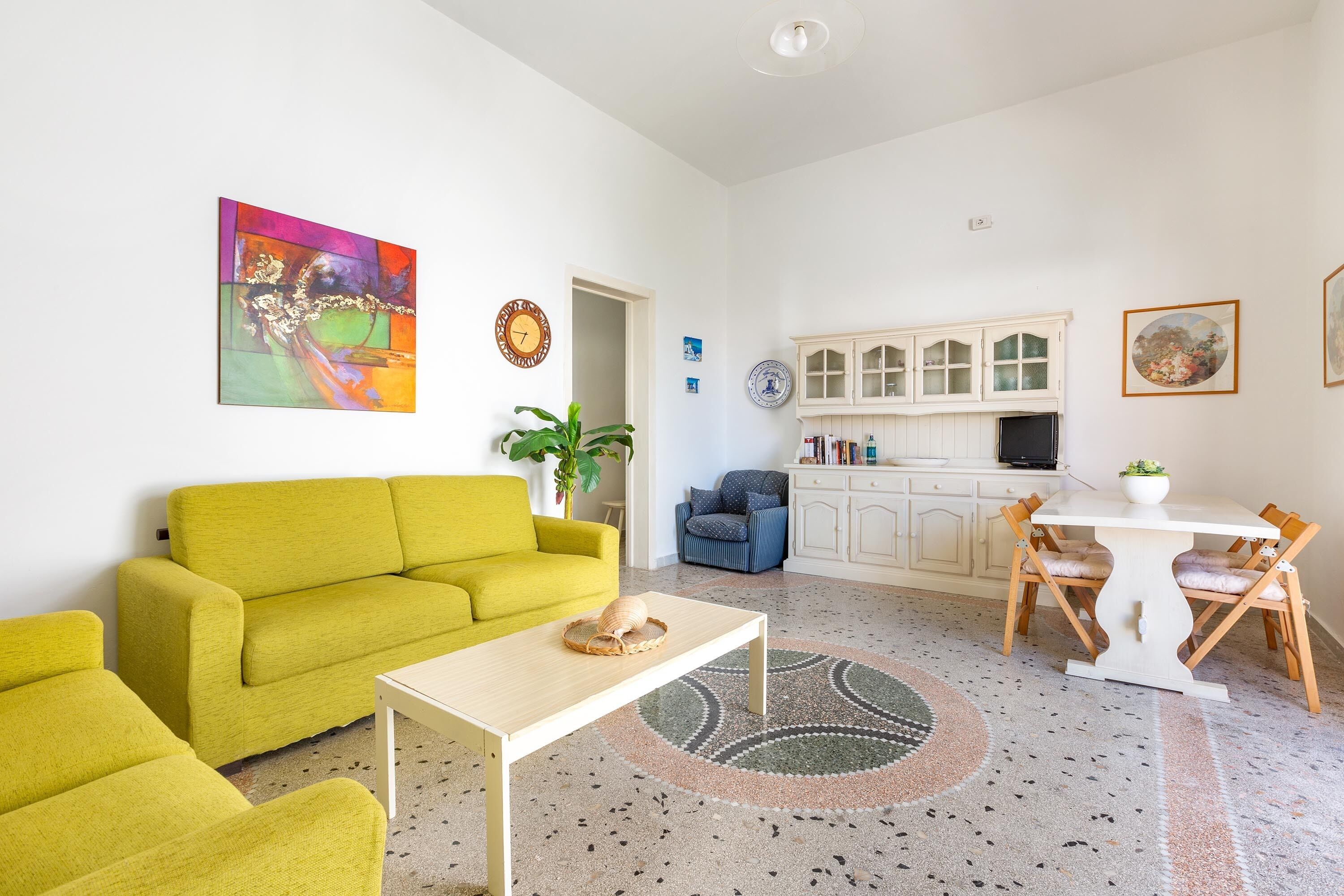 A living room with a yellow sofa, a coffee table, and a dining area with a white table and chairs.