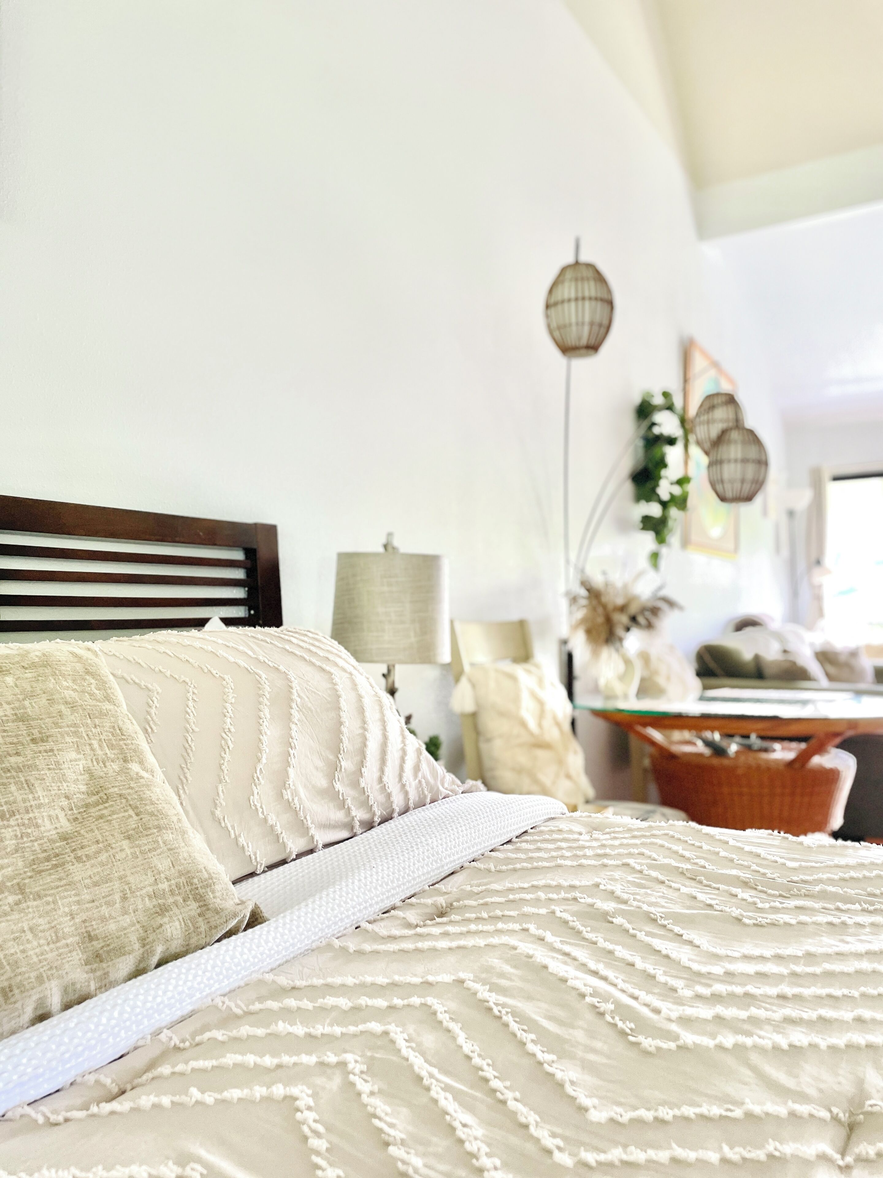 Una cama con cabecera de madera, una colcha blanca con textura y un plaid estampado.