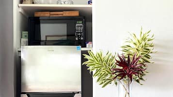 Une cuisine équipée d’un réfrigérateur, d’un four à micro-ondes et d’un petit meuble sur lequel se trouvent une horloge et quelques objets.
